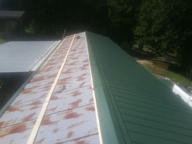 Old rusted panels beside newly installed green metal roofing — Wind Damage Roof Repair by Roofing Brothers in Moosup