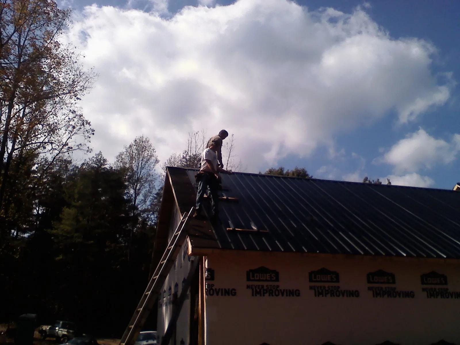 Roofer fastening dark metal panels high against a cloudy sky, from a Roof Inspection job in Moosup