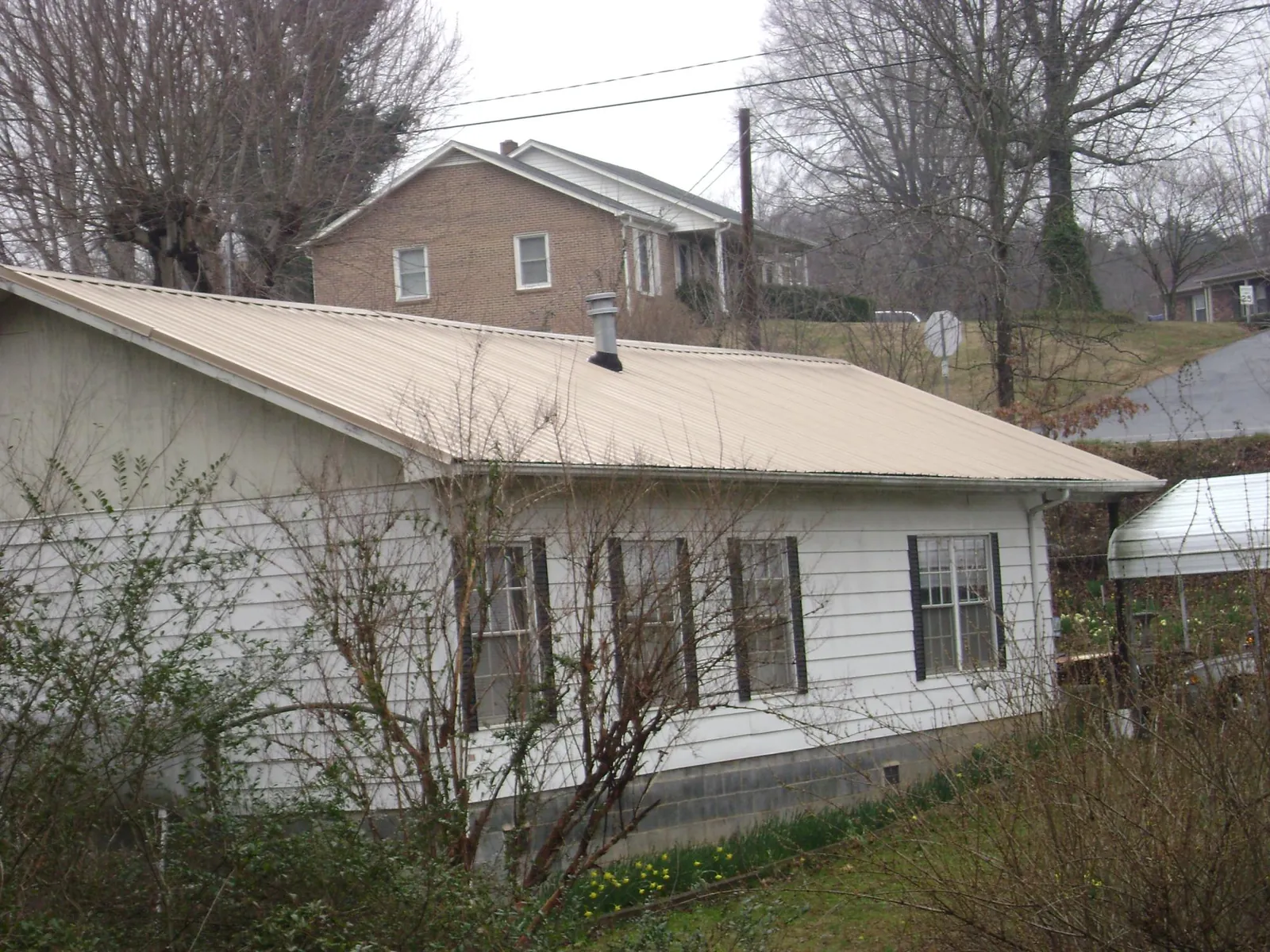 Tan metal roof on a white sided house set into a hillside — Commercial Roofing by Roofing Brothers in Moosup